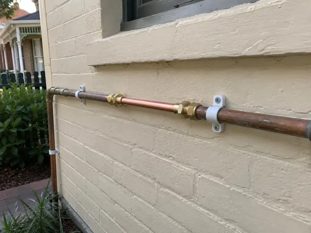 Repaired copper water pipe along an exterior brick wall beside a window in Dulwich Hill