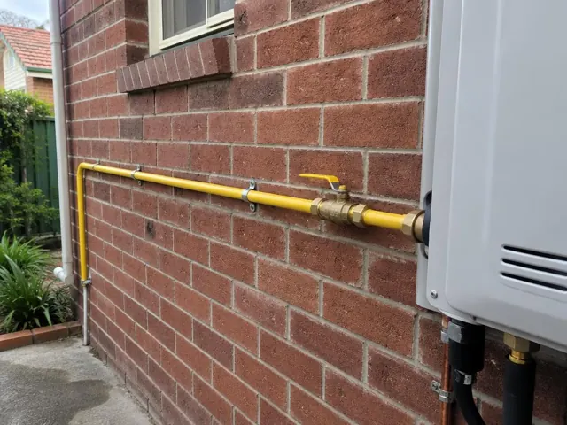 Yellow gas pipe and shutoff valve on a brick exterior wall beside a wall-mounted unit in Haberfield