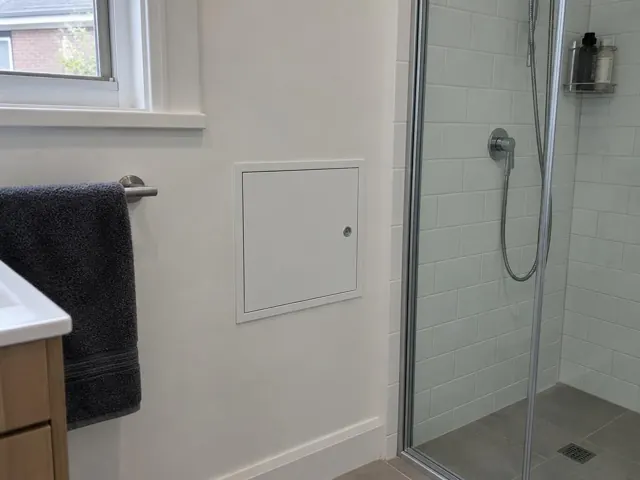 Bathroom wall with a small access panel beside a tiled shower and towel rail in Ashfield