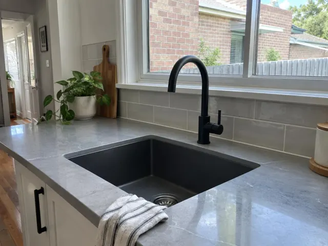 Black kitchen tap over a sink with grey benchtop and tiled splashback in Ashfield